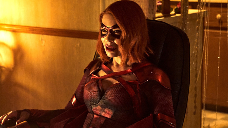 Crimson Countess in a red costume and eye mask sitting in a chair