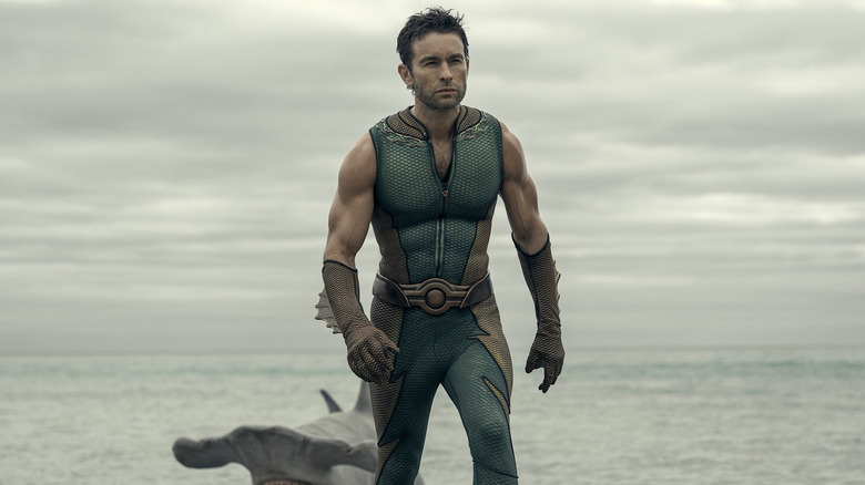 The Deep in a green suit walking away from the ocean with a hammerhead shark behind him in The Boys Season 5