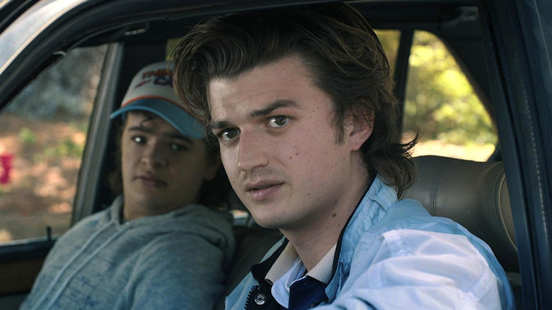 Steve Harrington in a blue shirt sitting in a car next to Dustin Henderson in Stranger Things