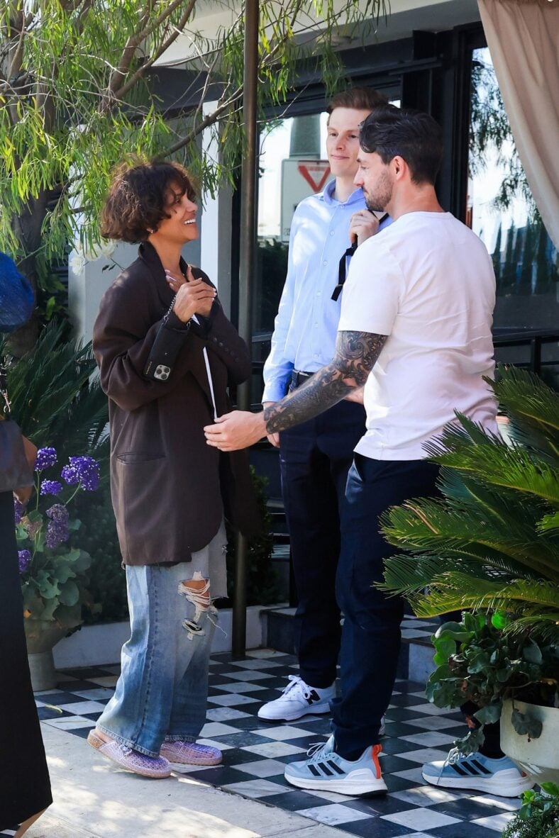 Halle Berry smiles while chatting with friends outside The Bird Streets Club, wearing an oversized brown blazer, white T-shirt, and jeans, during a lunch outing with fiance Van Hunt