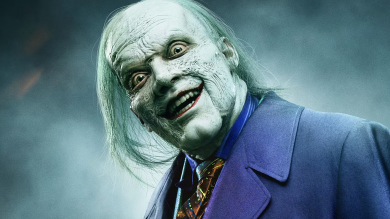 Cameron Monaghan as Jeremiah Valeska in Gotham, styled to look like the Joker with pale skin, green hair, red lips and a purple outfit.