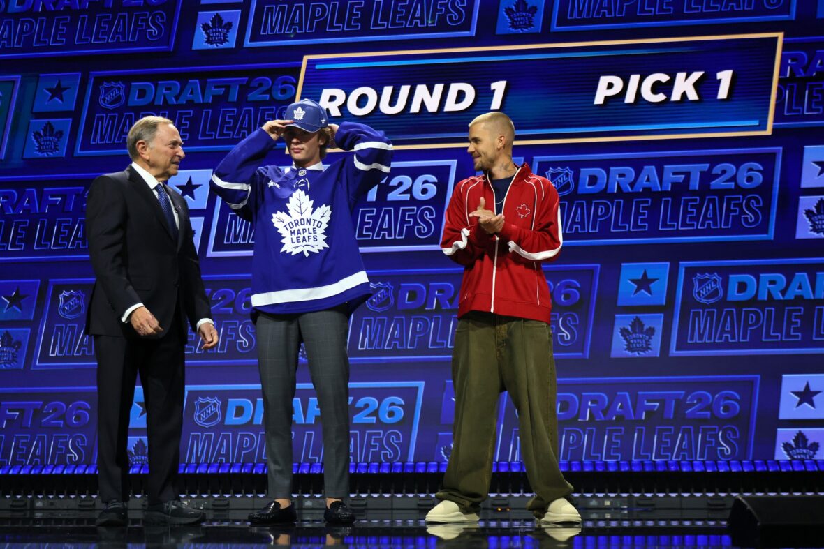 NHL commissioner Gary Bettman hands Gavin McKenna of Canada hat as singer Justin Bieber looks on after McKenna