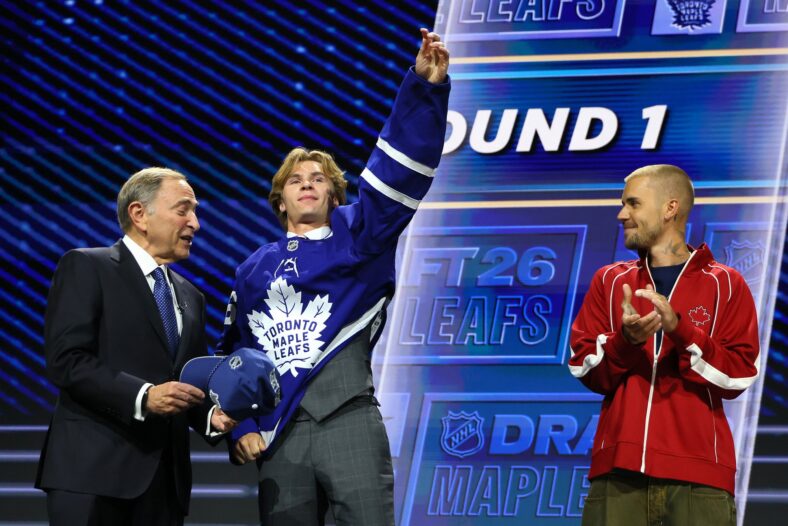 NHL commissioner Gary Bettman hands Gavin McKenna of Canada hat as singer Justin Bieber looks on after McKenna
