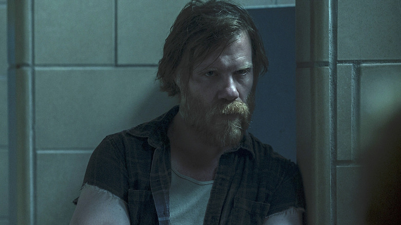 Russ Langmore in a ripped shirt leaning against a wall in Ozark