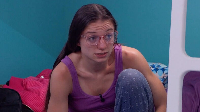 Mallory looking serious on Big Brother. She's in bed wearing a purple tank top