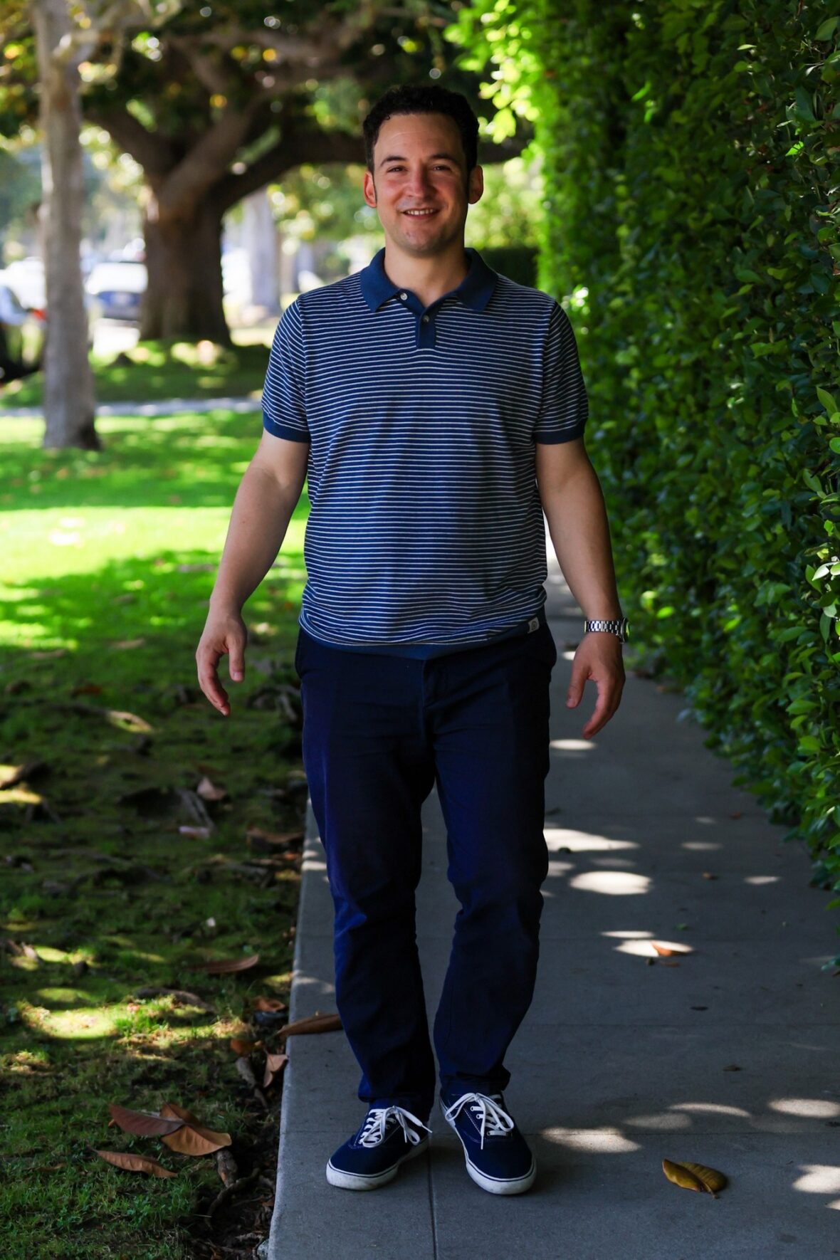 Ben Savage walking on a sidewalk in a striped polo shirt, smiling