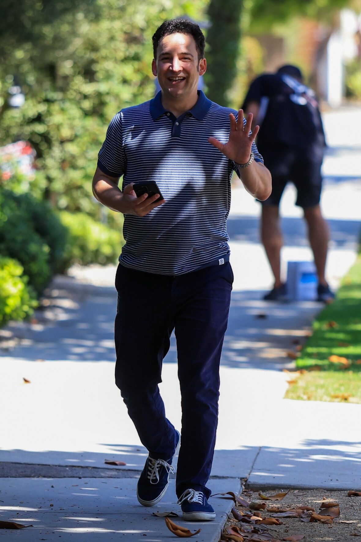 Ben Savage walking on a sidewalk in Santa Monica holding his cell phone and waving at a camera