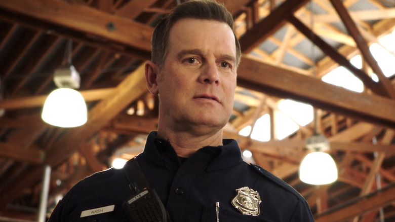 Bobby Nash in a dark blue uniform and badge looking downward in 9-1-1