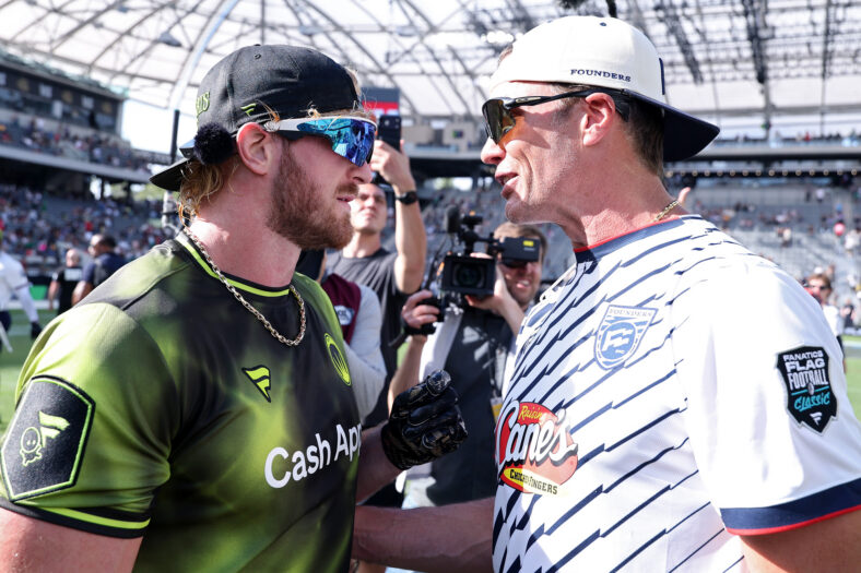Tom Brady and Logan Paul facing each other, both in sunglasses and backwards baseball caps, while having a tense moment