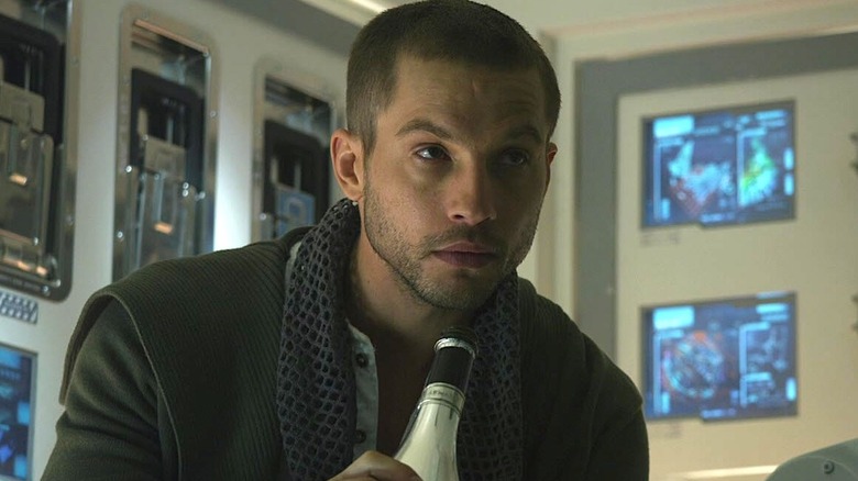 Charlie Holloway sitting in a spaceship room and holding a glass bottle