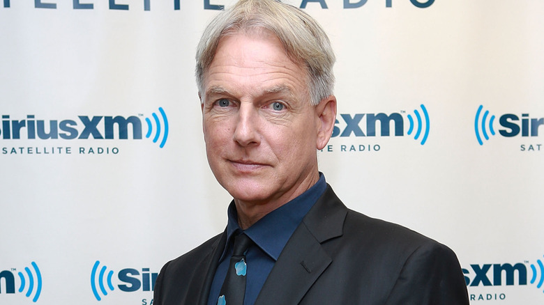 Mark Harmon in a black and blue suit and tie standing in front of a white and blue Sirius XM background