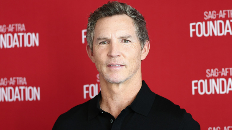 Shawn Hatosy in a black collared shirt looking straight ahead in front of a red background