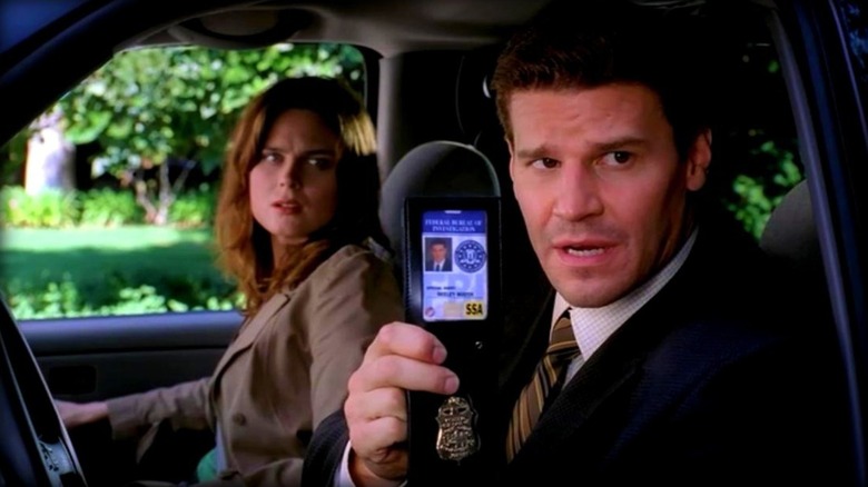 Seeley Booth showing his badge to someone while sitting in a car next to Dr. Temperance 