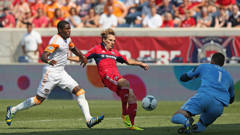Chris Rolfe #17 of the Chicago Fire takes a shot against Tally Hall #1 of the Houston Dynamo as Kofi Sarkodie #8 defends during an MLS match at Toyota Park on September 1, 2013 in Bridgeview, Illinois.