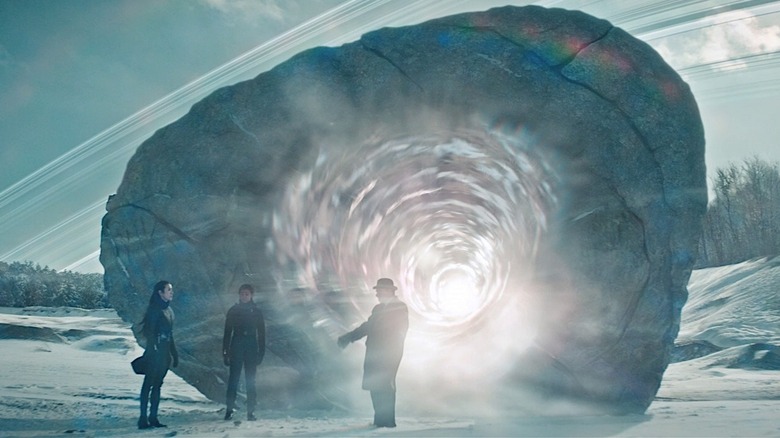 Three people standing in front of a huge rock and glowing portal on a snowy landscape in Star Trek: Discovery