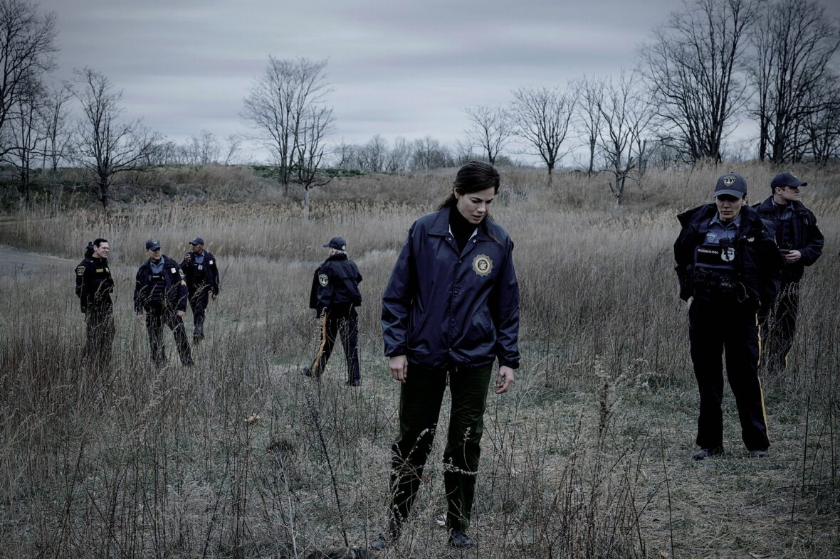 Michelle Monaghan leads a group of cops on a search through tall grass in a barren field in a still from