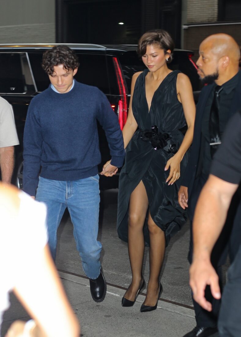 Tom Holland and Zendaya hold hands while walking together. Zendaya is in a black Ellie Saab dress.