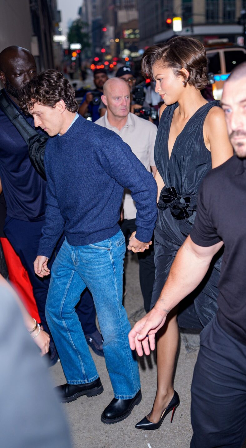 Tom Holland and Zendaya hold hands while walking together. Zendaya is in a black Ellie Saab dress.